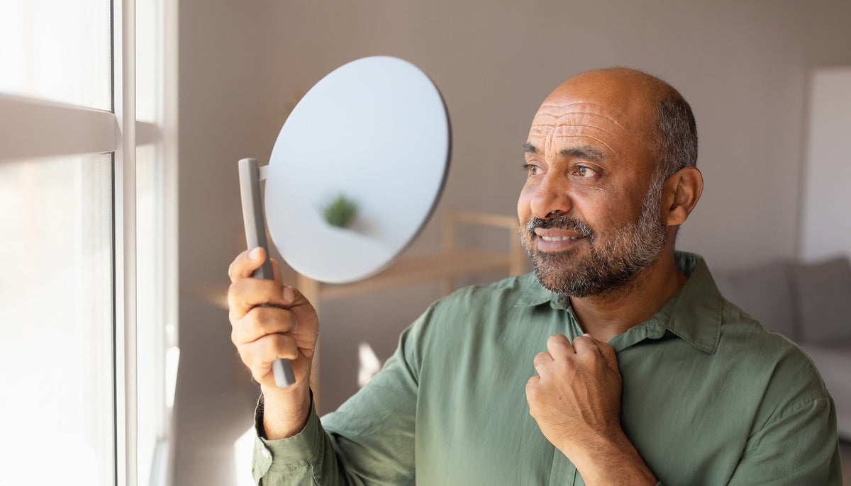 Adult man examining natural forehead lines in soft daylight near a window, shown from head to above the navel.